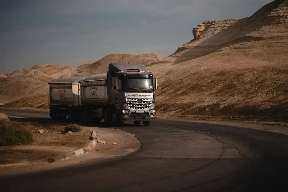 Седельный тягач с прицепом на извилистой дороге среди пустынных гор